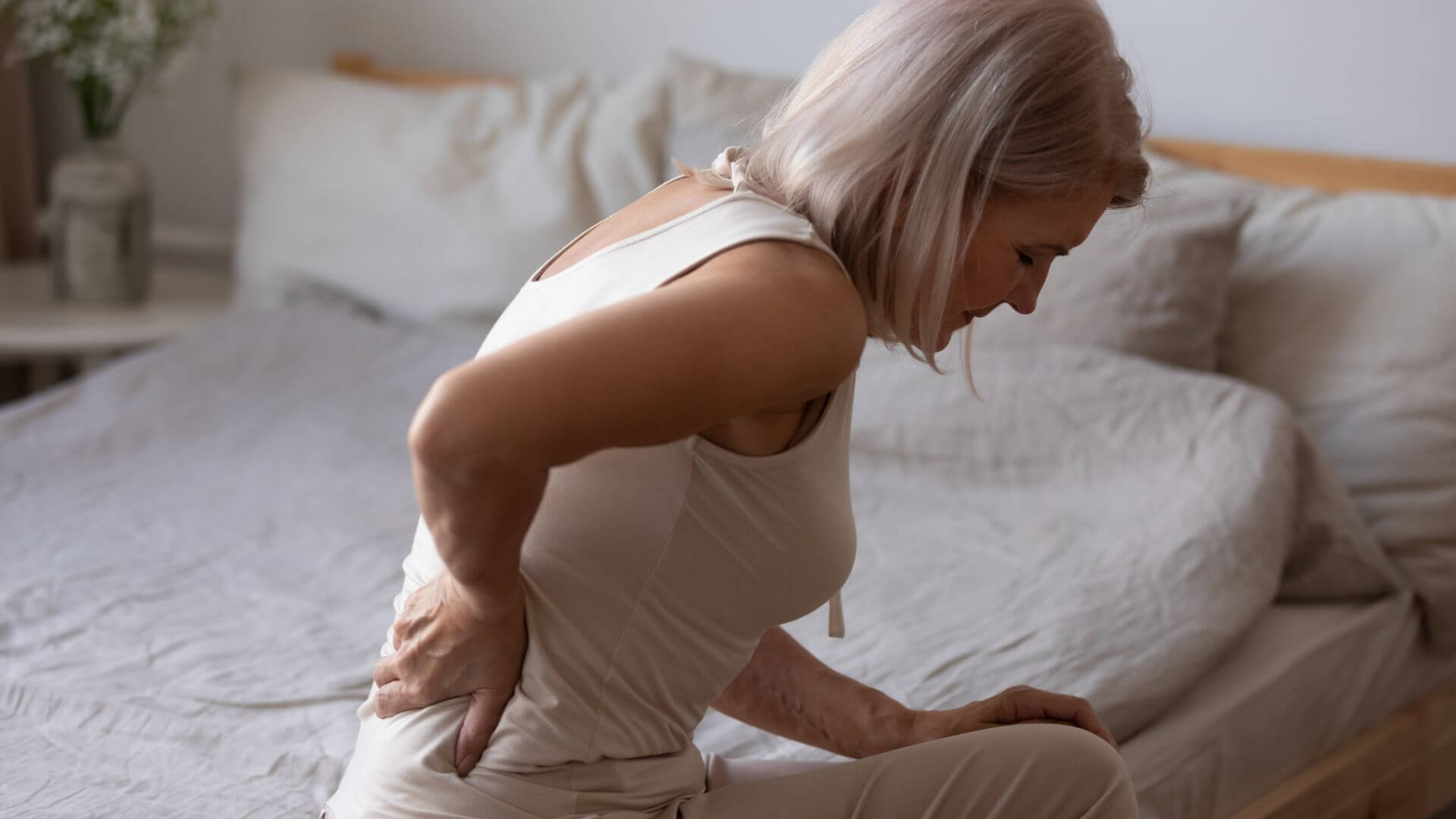 osteoporose-frau-mit-wirbelsaeulenschmerzen-sitzt-auf-bett-sanitaetshaus-wurst